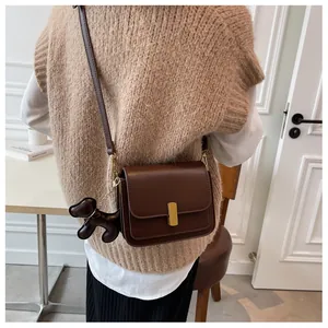 Détail d'un sac bandoulière marron foncé avec boucle dorée et breloque chien mignonne