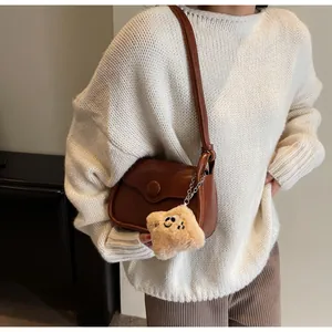 Brown vintage crossbody bag with decorative buckle and plush smiley charm on a model