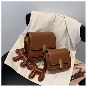 Détail de deux sacs bandoulière en cuir marron avec boucles dorées et breloque chien