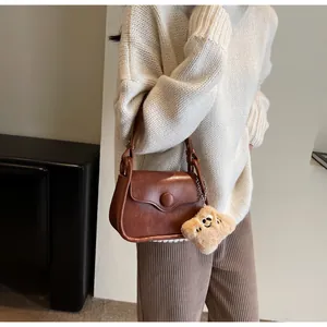 Detailed view of a vintage brown leather crossbody bag with a plush charm accessory