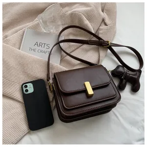 Détail d'un petit sac bandoulière marron foncé avec boucle dorée et breloque chien