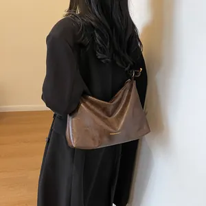 Grote minimalistische bruine hobo-tas van glanzend leer gedragen door een vrouwelijk model
