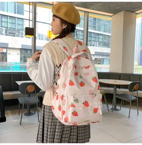Pink student backpack with strawberry print shown on model in a casual indoor setting