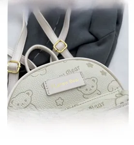 Detail eines cremeweißen Lederrucksacks mit Bärenprägung und goldenen Metallreißverschlüssen