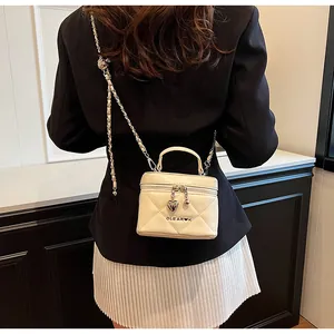 Close-up of cream quilted box bag with heart pendant zipper and chain strap detail