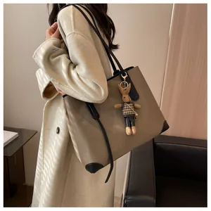 Close-up of khaki tote bag with black handles and cute rabbit charm on an elegant coat