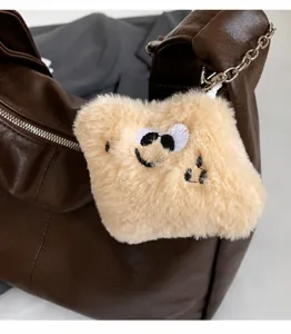 Close-up of a smiling plush charm pendant on a vintage brown leather tote bag