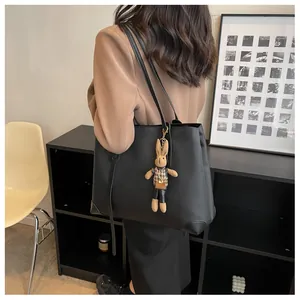Detail of a large black tote bag featuring a stylish checkered rabbit doll charm and strap