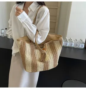 Dettaglio di una grande borsa in paglia a righe verticali, nappa e manici intrecciati
