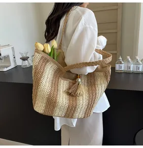 Dettaglio di una borsa da spiaggia in paglia a righe con nappa e manici intrecciati