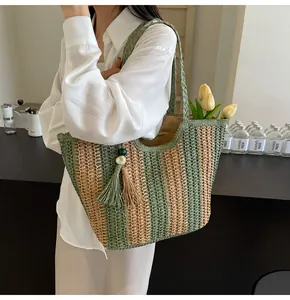 Dettaglio di una borsa da spiaggia in paglia a righe con ciondolo a nappa di perline verdi