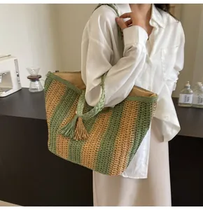 Dettaglio ravvicinato di una grande borsa tote in paglia a righe con nappine in casa