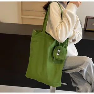 Detalle del bolso tote de lona verde con bordado de ojo de monstruo y mini neceser a juego