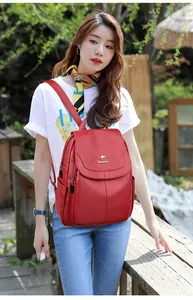 Detail of red pebbled leather backpack showing flap closure and metal logo accents