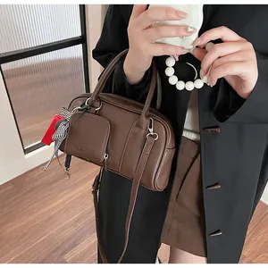 Detail of dark brown Boston bag with smooth texture, mini pouch, and striped ribbon