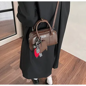 Detail of dark brown Boston bag with creative charms and mini pouch on leather shoulder strap