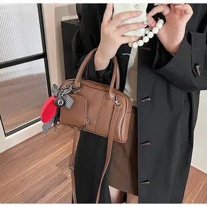 Detailed view of a brown leather crossbody bag with dual handles and decorative charms