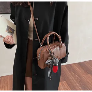 Detail of brown leather bag with elegant bow charm and round handles in a soft indoor setting