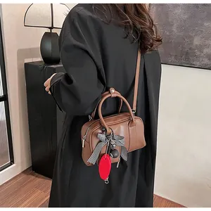 Detail of a brown leather crossbody bag with striped bow pendant in a modern studio