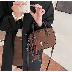 Brown suede handbag featuring dachshund appliqué and decorative charms on a model