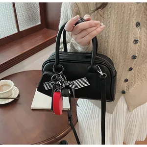 Detail of black crossbody bag with checkered bow and heart pendant on a wooden table