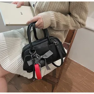 Detail of black Boston bag with a checkered bow, red charm, and silver-tone hardware accents