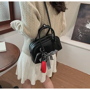 Close-up of black crossbody bag with check pattern bow and red charm detail on a model