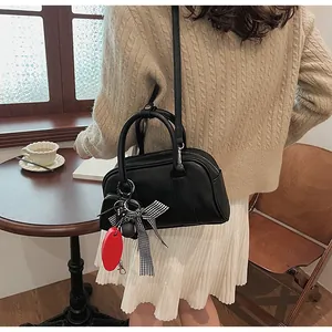 Detail of black leather Boston bag with checkered bow charm in a cozy cafe setting