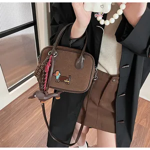 Close-up of brown suede handbag with dachshund embroidery and chocolate charm