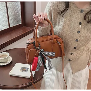 Detail of brown faux leather Boston bag with decorative bow and red charm on a desk
