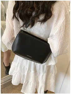 Détail d'un sac bandoulière minimaliste en cuir noir mat porté sur une robe blanche