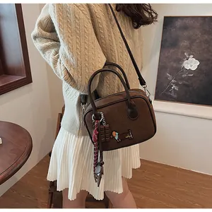Close-up of brown suede handbag featuring dachshund patch and chocolate pendant detail