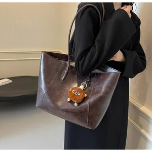 Détail d'un cabas en cuir marron foncé avec charm monstre en peluche et fines bandoulières