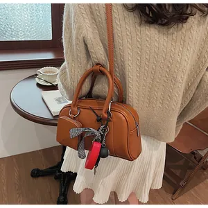 Close-up of a brown Boston bag with heart charms and bow detail in a cafe setting