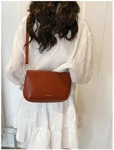 Vue détaillée d'un sac à bandoulière en cuir caramel porté sur une robe blanche