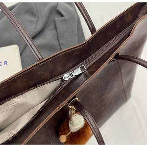Détail d'un sac cabas marron foncé montrant la fermeture zippée et le pendentif pompon