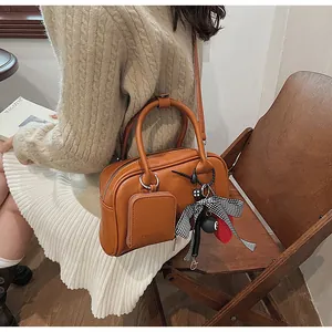 Detail view of brown leather handbag featuring a plaid bow and detachable mini pouch
