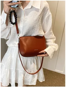 Petit sac bandoulière en cuir caramel au design minimaliste porté sur robe blanche