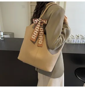 Detail of khaki pebbled leather tote bag with a brown checkered silk scarf on the handle