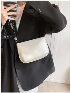 Détail d'un sac à bandoulière en cuir crème avec boucles argentées sur veste noire