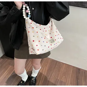 Detail of canvas tote bag featuring colorful polka dots and beaded heart charm shoulder strap