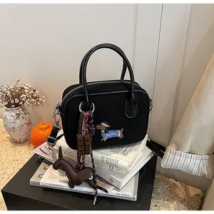 Close-up of black canvas handbag featuring dachshund embroidery and unique charm accessories