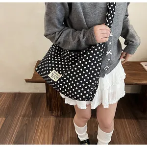 Detailed view of large black and white polka dot canvas crossbody bag with brand label