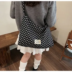 Back view of a large black canvas crossbody bag with white polka dots on a grey sweater