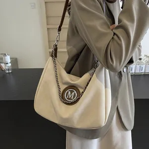 Sac bandoulière rétro en daim beige et cuir marron avec chaîne porté par mannequin