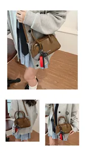 Detail of brown bowling bag with CLEAR K logo, detachable strap, and plaid scarf accessory
