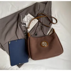 Détail du sac à bandoulière marron foncé avec logo M et chaîne argentée sur blazer gris