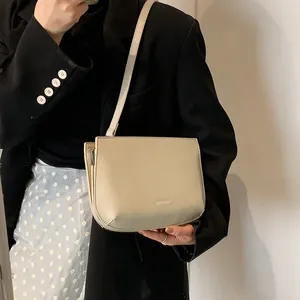 Sac sous le bras élégant en cuir crème pour femme porté avec un blazer noir chic