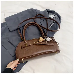 Detail view of brown leather retro shell bag with gold hardware and baseball charm