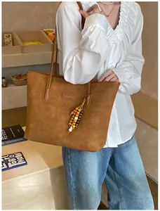 Detail of a large brown tote bag with textured finish and decorative beaded charm